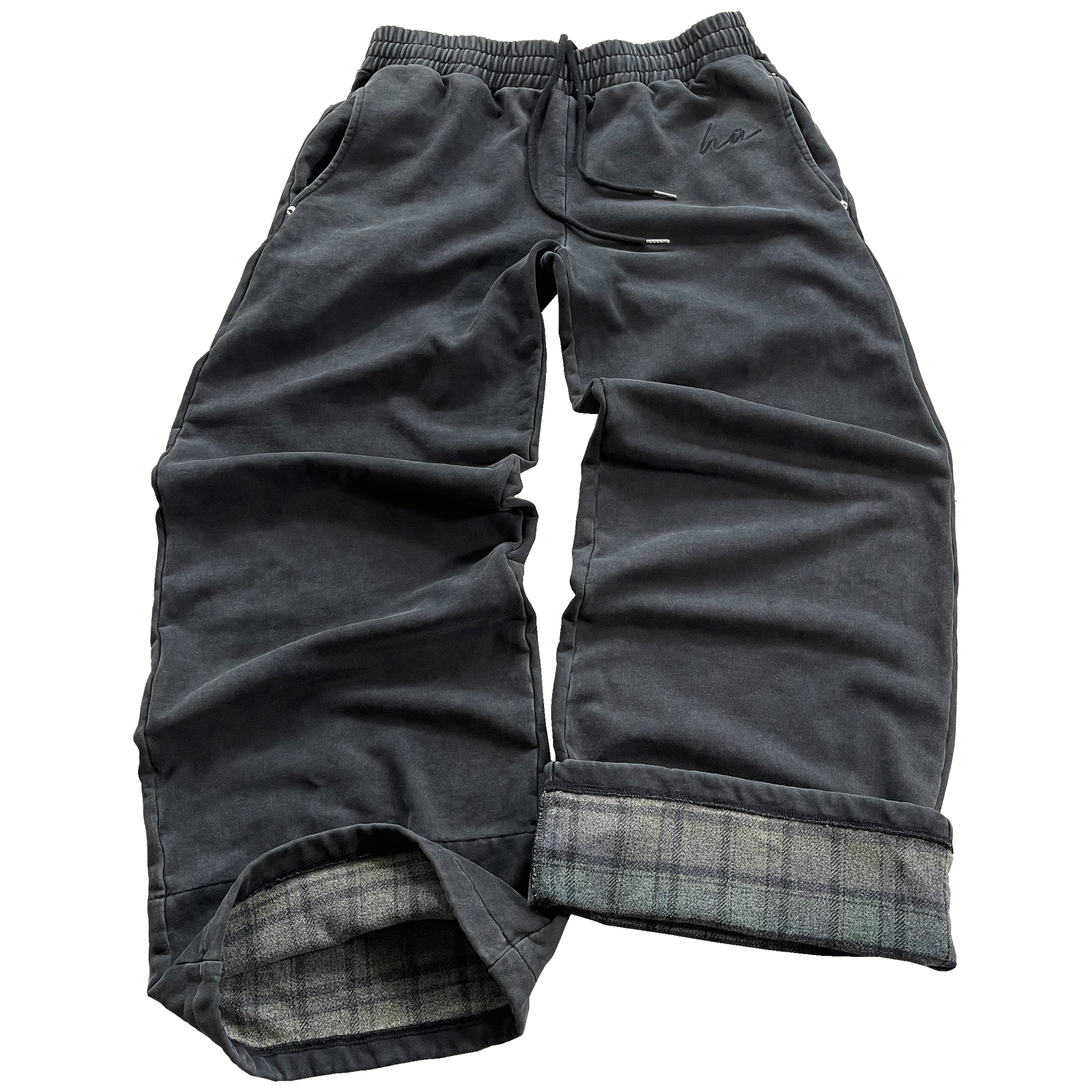 A pair of black joggers with plaid patterns on the pockets and inside near the ankles, featuring an oversized fit and curved pockets with metal rivets. Embroidery is visible on the left pocket area.