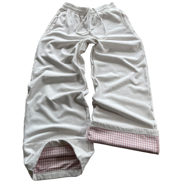 A pair of white and pink color sweatpants with houndstooth pattern on pockets and inside near ankle, featuring an oversized fit and curved pockets with metal rivets.